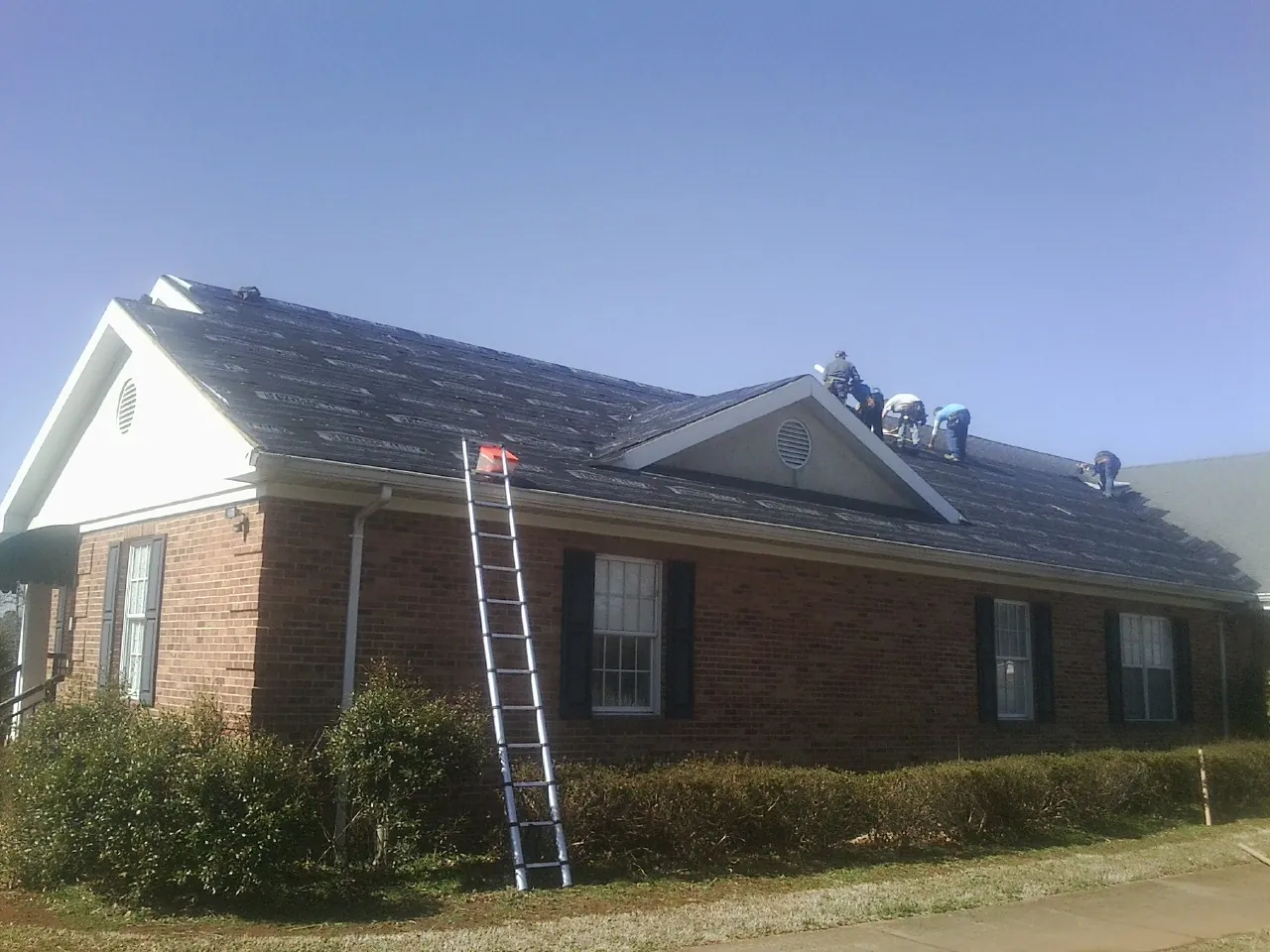 Crew tearing shingles off a brick ranch roof with a ladder set — Emergency Roof Repair work by our crew in Newtown
