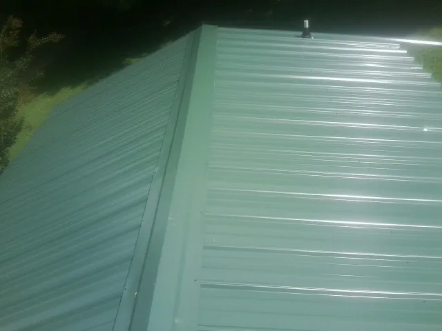New green metal panels meeting at the ridge of a roof — Flat Roof Repair work by our crew in Newtown