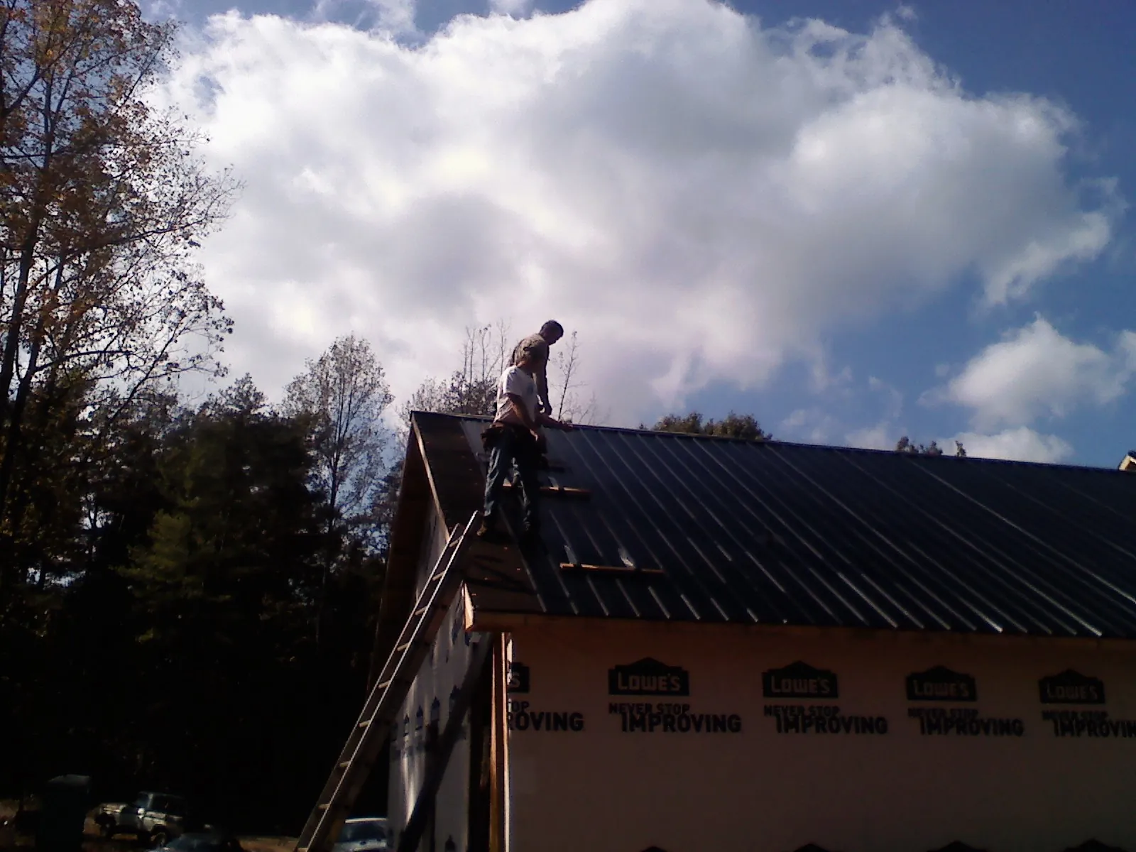 Roofer fastening dark metal panels high against a cloudy sky, from a Roof Inspection job in Newtown