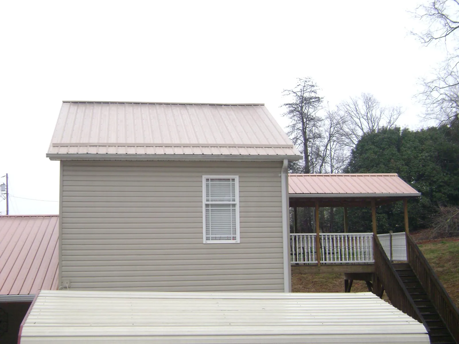Tan metal roofs on a two story addition and attached porch, from a Roof Replacement job in Newtown
